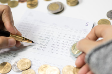 Hand holding gold pen and coins on bank account passbook. Concept of money saving and financial....