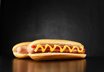 Two big hotdogs with sausages, mustard and ketchup isolated on black background. Top view.