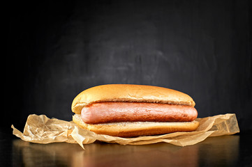 Plain hotdog with big sausage on kraft paper isolated on black background. Top view.