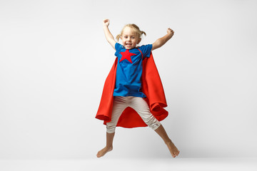 Very excited little girl dressed like superhero jumping alongside the white wall. © Maksim Kostenko