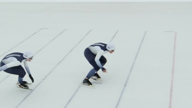 High angle shot with slowmo of professional sportswomen in spandex full-body covering suits speed skating in ice rink