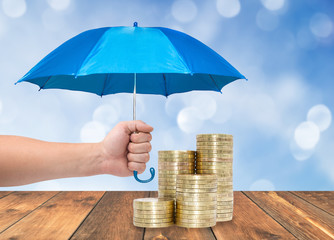 Coins under a blue umbrella protection money concept 