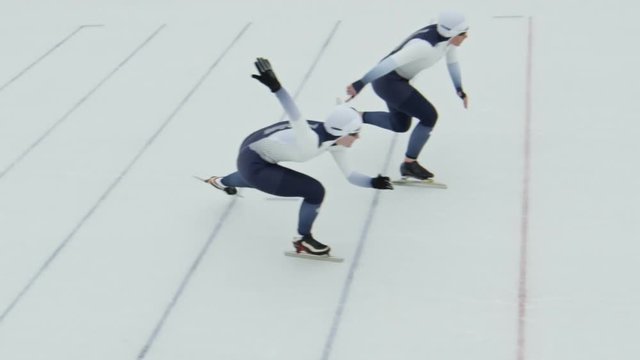 High angle shot with slowmo of female speed skaters in professional sportswear competing during practice in ice rink