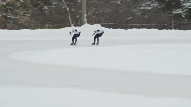 Tracking of professional athletes in spandex full-body covering suits speed skating along track in outdoor ice rink