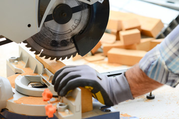 close up detail of manual worker hands using a power tool circular saw