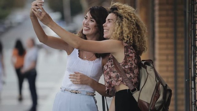 Urban style happy two women friends make selfie pictures by smartphone in city street, slowmotion