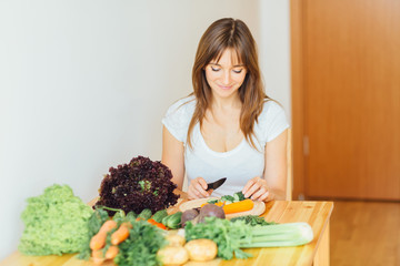 Young beautiful woman cutting vegetable for smoothie or soup in kitchen. Healthy eating, cooking, food, dieting and people concept.