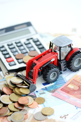 Red agricultural tractor, cash money and calculator suggesting professional financial support