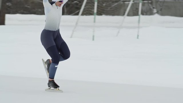 Tracking with slowmo of professional female speed skater winning race against teammate during practice in outdoor ice rink in winter