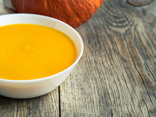 white plate with pumpkin orange soup on wooden aged background with empty space for your text