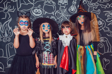 Children in scary Halloween costumes stand against a wall with drawings.