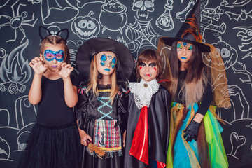 Children in scary Halloween costumes stand against a wall with drawings.