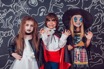 Children in scary Halloween costumes stand against a wall with drawings.