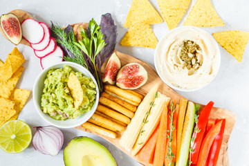 Hummus and guacamole with vegetables and snacks on a wooden board