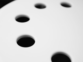 Perspective close up part of white large grainy texture plastic round disk, with orderly arranged black holes in circle, abstract background