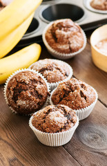 Homemade banana chocolate muffins sprinkled with sugar on a wooden background.