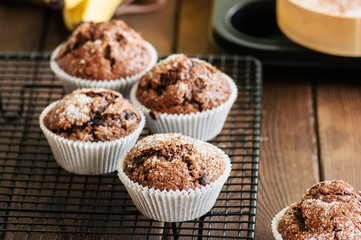 Homemade banana chocolate muffins sprinkled with sugar on a wooden background.