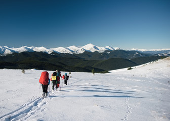 Group of tourists walks on a mountain hill in winter. Mountain range covered with snow at the background
