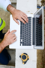 close up detail of a foreman architect hands working on laptop computer in new house construction site