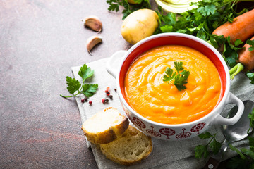 Carrot and pumpkin cream-soup on dark table.