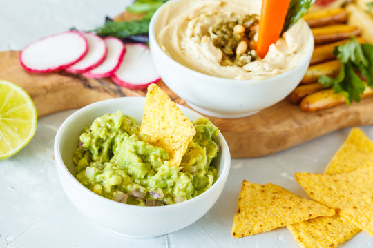 Hummus and guacamole with vegetables and snacks on a wooden board