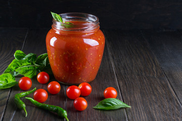 Spicy sweet tomato sauce with garlic, pepper and herbs in a glass jars.