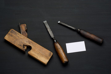 Woodworking tool on dark wooden background. chisel, plane and empty business card.