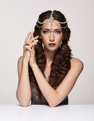 Fototapeta premium Beauty portrait of young woman in pearl diadem. Brunette girl with braids hairdo and day female makeup sit at white table
