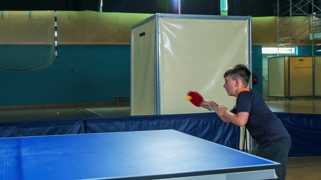 A young boy is focused when playing table tennis in a school gym. He is really enjoying it.