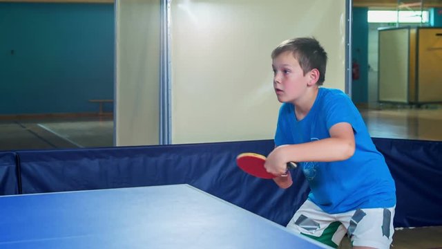 Boys and girls are playing table tennis during their PE class in a school gym. They really like it.