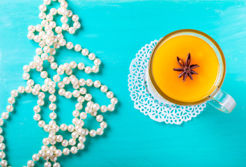 Naklejka premium Glass of sea buckthorn beverage (kissel) and pearl beads on a bright blue wooden table or board for background. New year theme