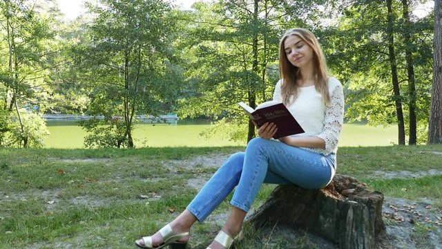 4k.Young modern girl reads  Bible in  summer park. Christian  belief. Slider