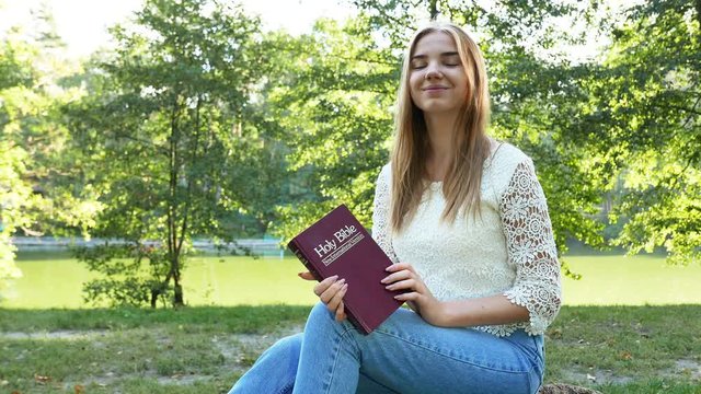 4k.Young girl with Bible in  summer park look forfard. Christian  belief. 