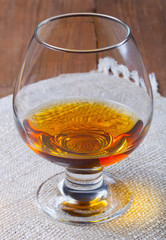 Cognac in a glass goblet on the old wooden table and linen napkin. Selective focus