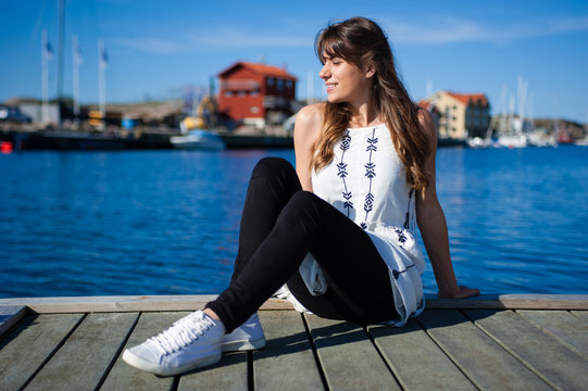 Young and happy tourist woman sitting in the harbor on wood pier