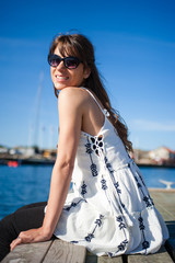 Young and happy tourist woman sitting in the harbor on wood pier