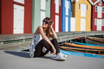 Young and happy tourist woman sitting in the harbor in Smogen town, Sweden. Beautiful traditional colorful wood houses on the background.