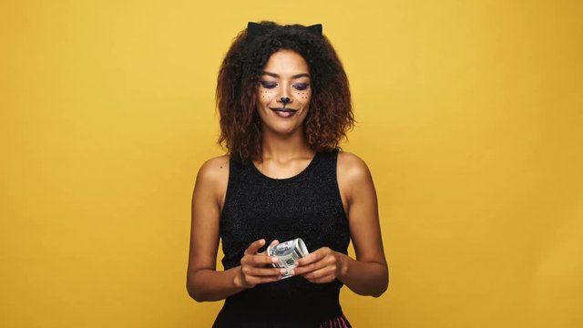 Young african tricky woman counting cash and hiding money isolated over yellow background