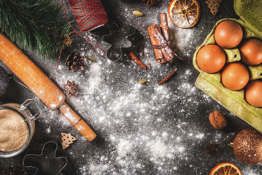 Christmas, New Year holiday cooking background. Ingredients, spices, dried oranges and baking molds, Christmas decorations (balls, fir-tree branch, cones), On black stone table, copy space top view