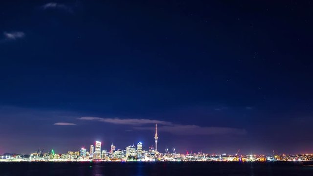 Time lapse of a starry sky above Auckland city’s skyline with the harbour, the ocean and some boats at the front