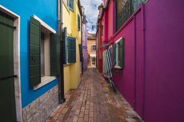 Beautiful colorful house facades on Burano island, north Italy. Narrow street with colorful houses (blue,magenta,yellow,red)