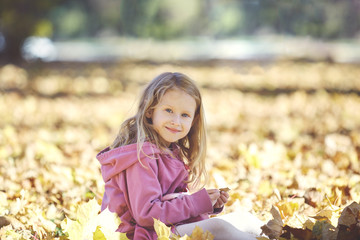 happy little girl laughing and playing with leaves in the autumn on the nature walk outdoors