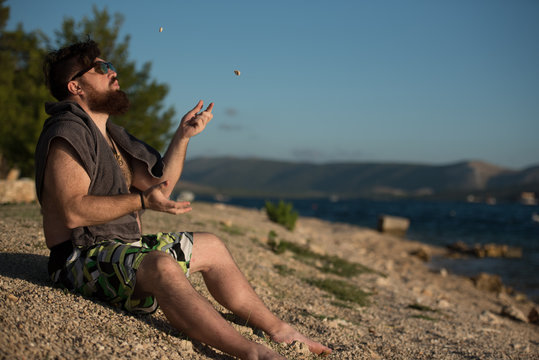 young man sitting on beach and playing with small rocks 