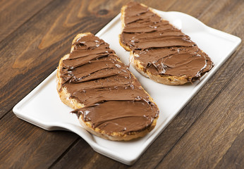 Chocolate spread on bread on a plate over brown wooden table. Food.