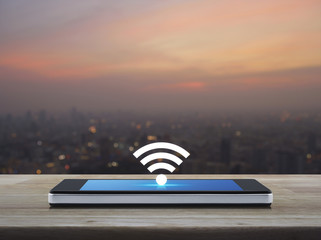 Fototapeta na wymiar wi-fi button flat icon on modern smart phone screen on wooden table over blur of cityscape on warm light sundown, Technology and internet concept
