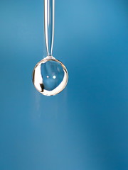 Goccia d'acqua brillante a forma di pallina che sta per staccarsi su sfondo blu.