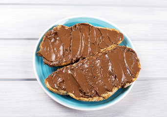 Chocolate spread on bread on a blue plate on wooden table.
