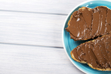 Chocolate spread on bread on a blue plate on wooden table. Copy space.