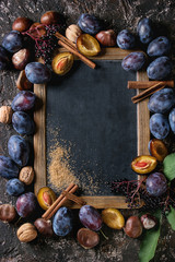 Autumn frame from plums, nuts, cinnamon and brown sugar with empty vintage chalkboard over brown concrete background. Top view with space for text. Fall harvest and jam making concept.