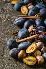 Autumn plums, nuts, cinnamon over brown concrete background. Close up with space for text. Fall harvest and jam making concept.